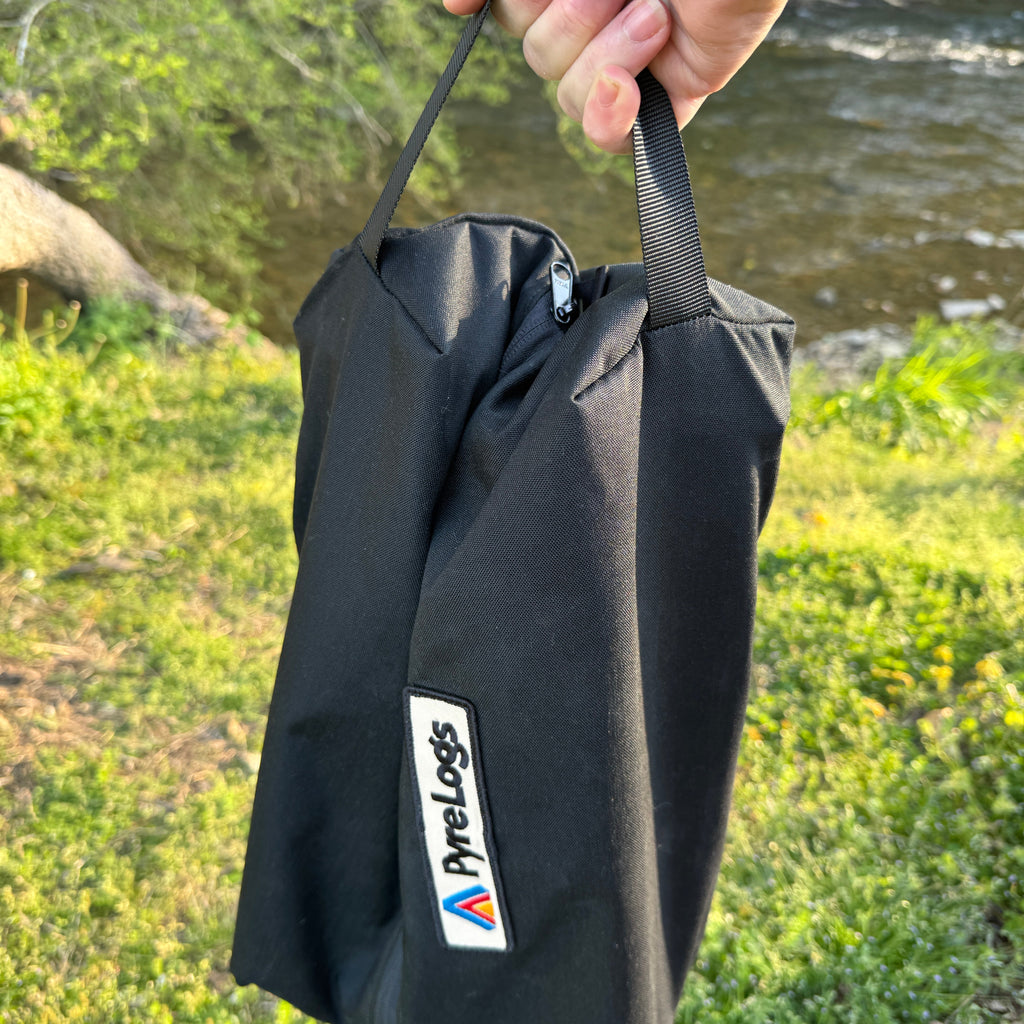 Black log carrier with PyreLogs logo held by a hand against a natural background