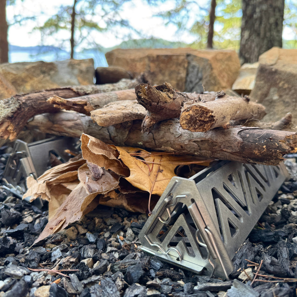 Metal fire pit grate on a campfire with wood and stones in the background